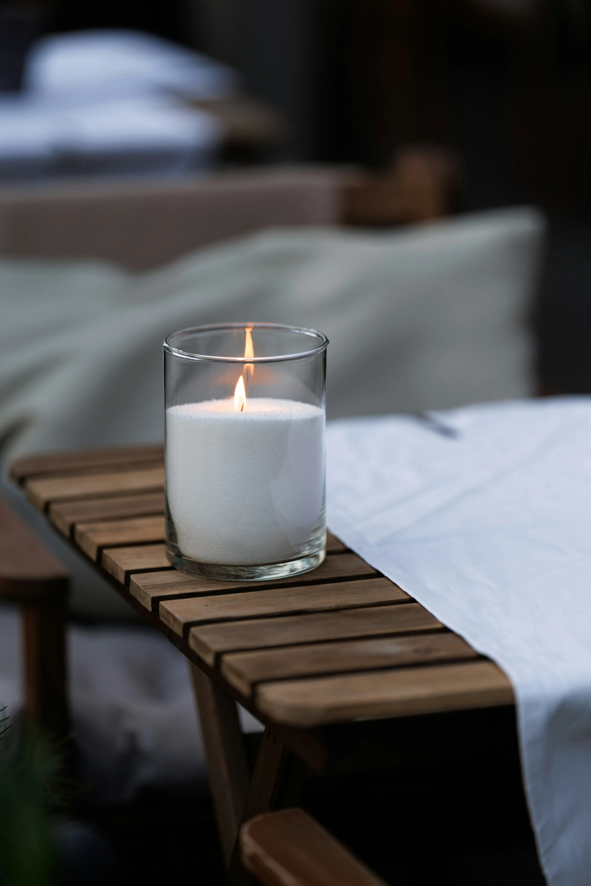 Vela acesa em recipiente de vidro sobre uma mesa de madeira.