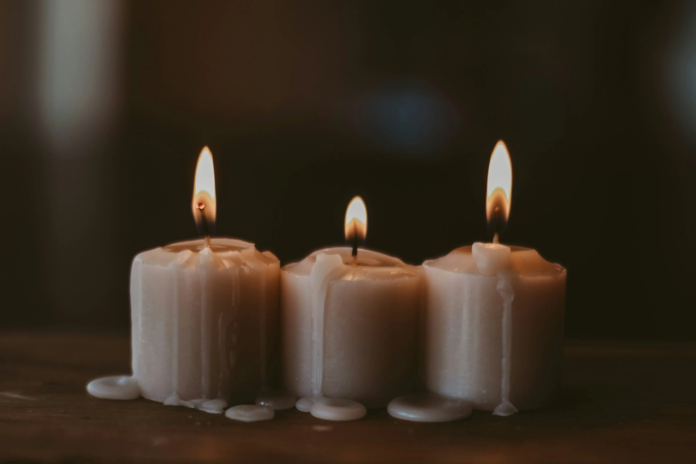 Três velas claras acesas, com detalhes de cera e luz suave.